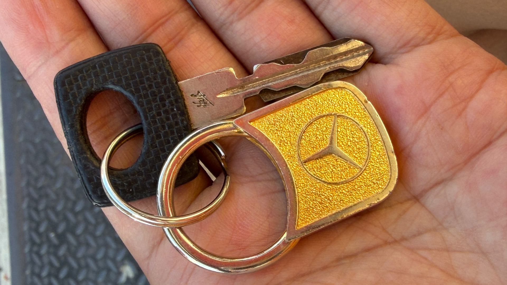 Older Mercedes-Benz key with gold fob in a technician's hand